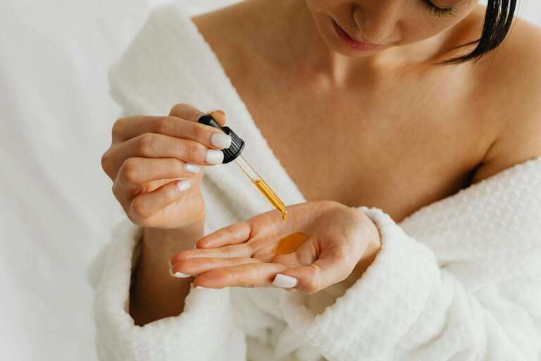 Woman in bathrobe applying oil to hands, representing Abhyanga self-massage for healthy skin and holistic well-being in Ayurveda