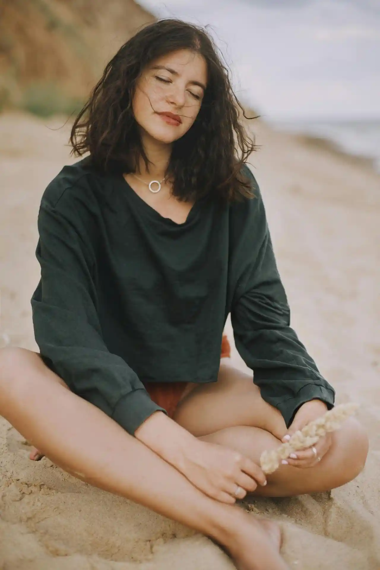 Woman sitting calmly on the beach with her eyes closed, appearing serene and at peace during the 5-Day Digestive Reset.
